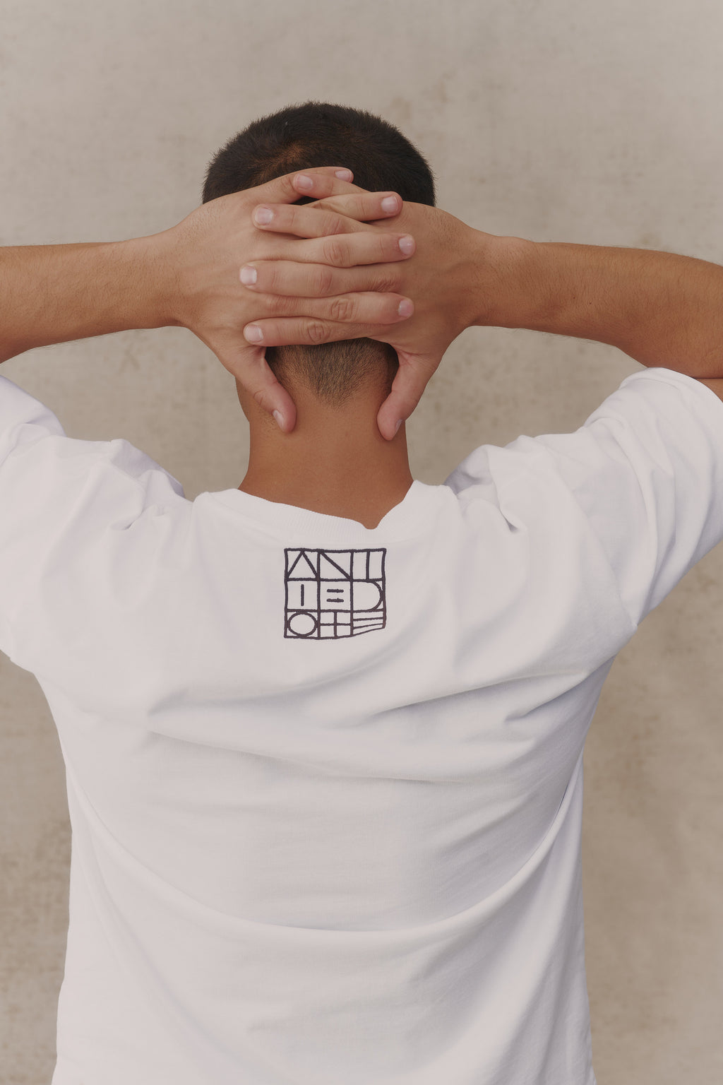Man wearing the Antidote Reset Tee in Crisp White, close-up of the back logo