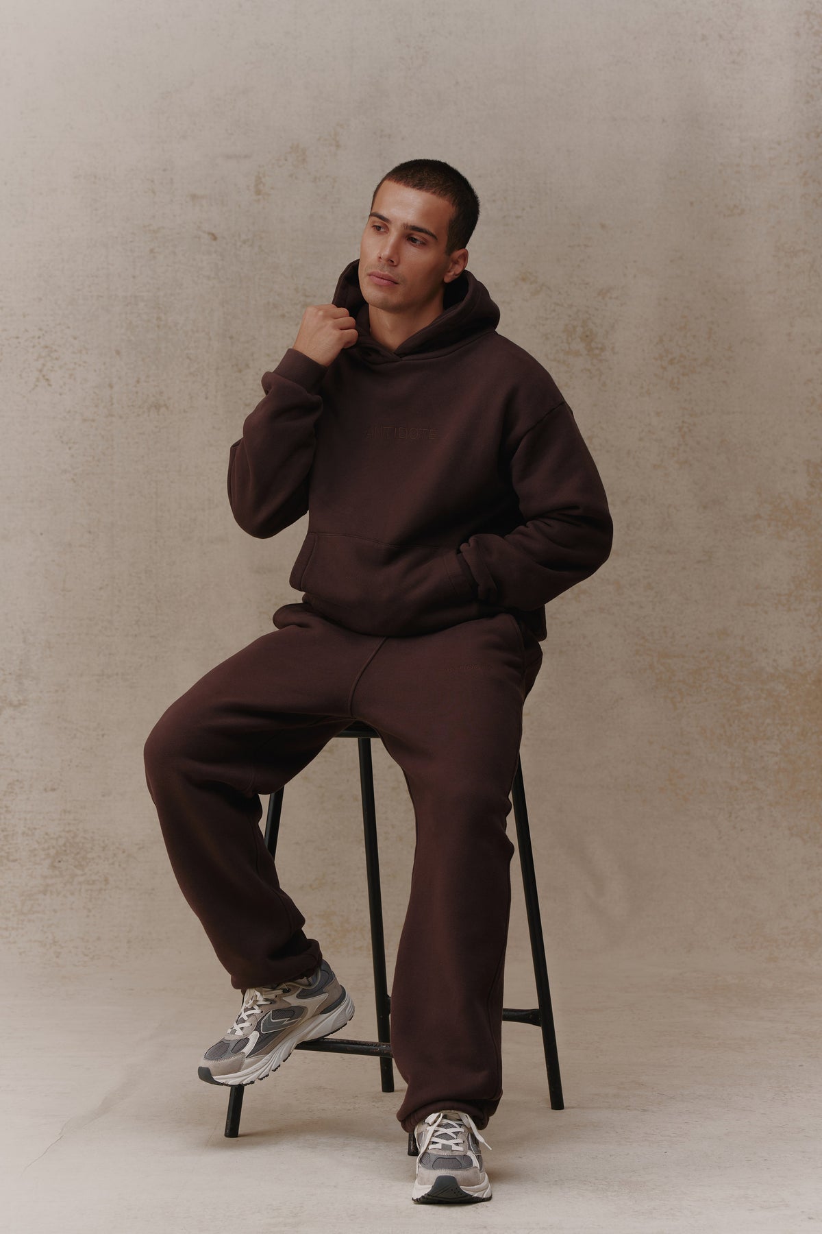 Man wearing the Antidote Men's Restore Joggers in Ganache, seated on a stool