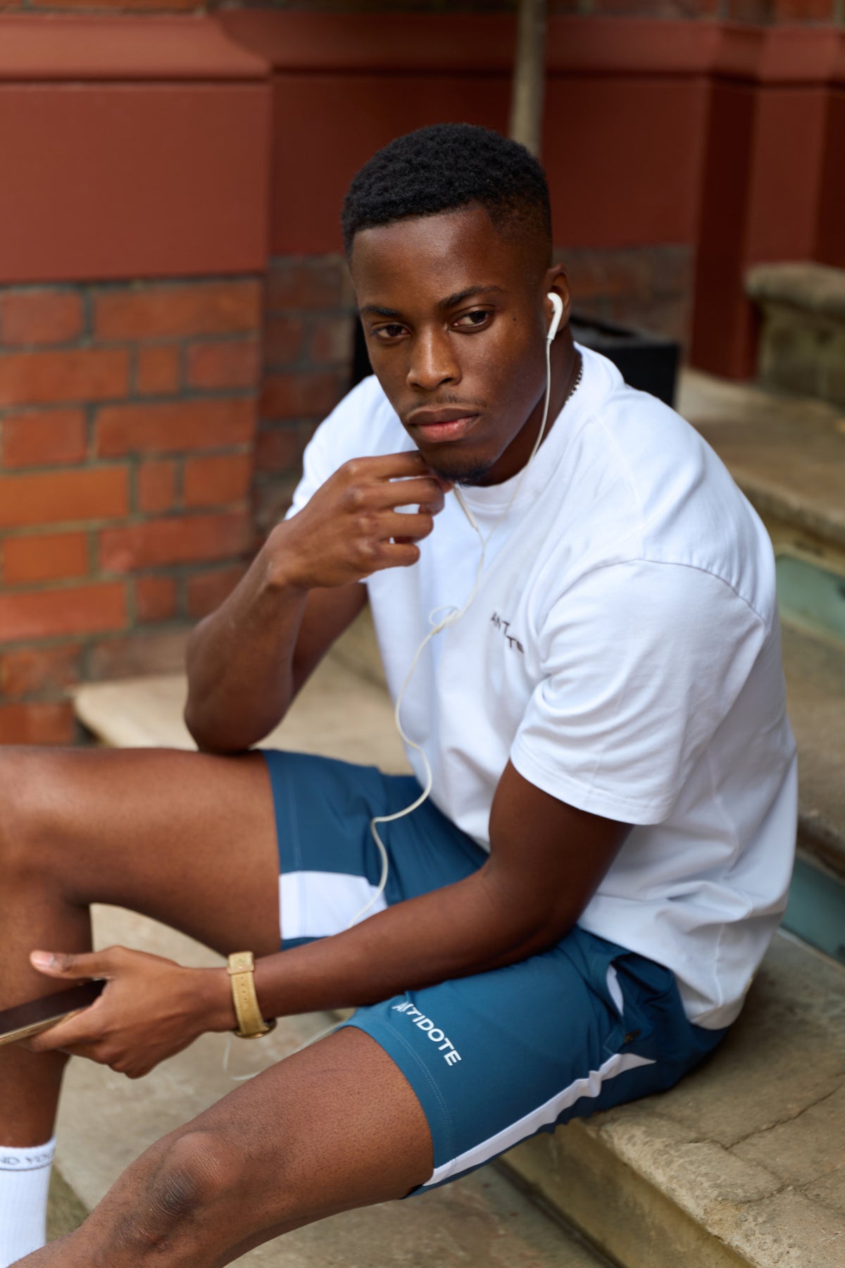 Man wearing the Antidote Motion Men's Shorts 5 inch in Ocean Blue, sitting on a step